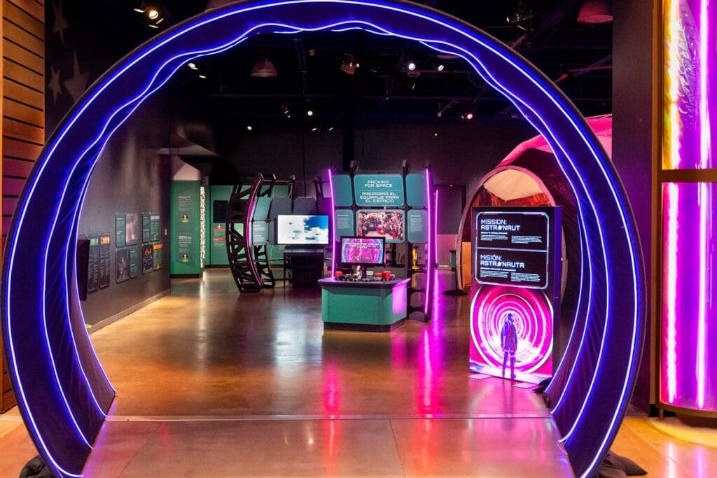 A museum exhibit featuring a large, circular neon-lit archway and interactive displays with informational panels in a modern, brightly lit room, perfect for touring exhibition companies seeking memorable experiences.